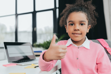 Wall Mural - Adorable little girl showing thumb up sign and smiling at camera