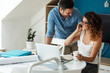 © BalanceFormCreative - Woman buying online stocks actions. She's using laptop and speaks on phone while her husband stands beside and support her.