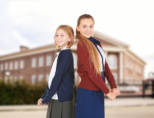 Wall Mural - Two cute girls in school uniform on white background