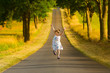 Kleines Mädchen in Sommerkleid läuft springend und jubelnd eine Straße entlang und freut sich an einem warme Sommerabend - Pure Lebensfreude!