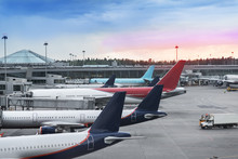 Tails Of Some Airplanes At Airport During Boarding Operations. They Are Four Planes On A Sunny Evening, With A Blue Red Sky. Travel And Transportation Concepts.