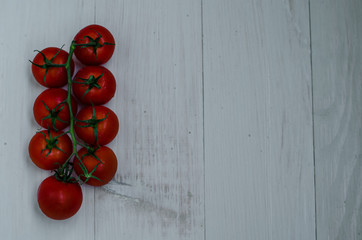 A branch of red organic cherry tomatoes on a wooden background