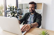 © LIGHTFIELD STUDIOS - Smiling bearded man in headphones using laptop while sitting at table