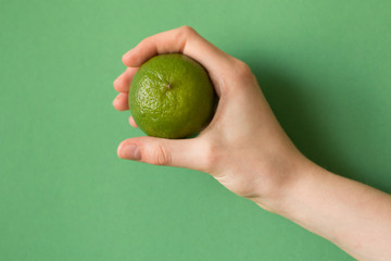 Fresh juicy tasty green lime in a human hand on green background