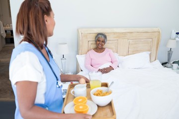 Wall Mural - Female doctor serving breakfast to senior woman on bed