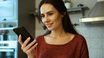 Attractive caucasian woman using smart phone device, surfing internet, reading recipe on her kitchen. Close up