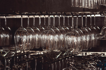 Wall Mural - raws of glasses for a margarita, martini, grog and liqueur hanging upside down in bar at arestaurant, dark background.