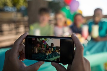 Cropped hand of person photographing children through mobile pho