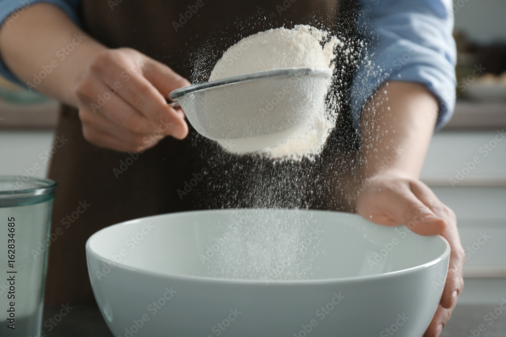Human hands sifting flour into ceramic bowl, closeup