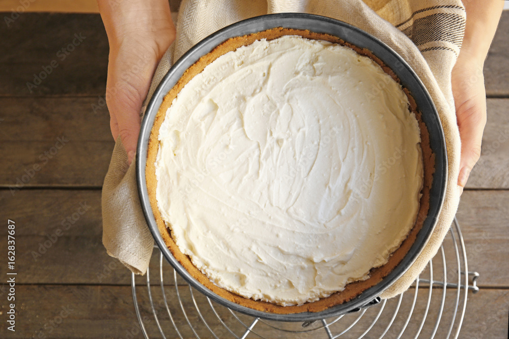 Woman holding baking pan with raw cheese cake in kitchen