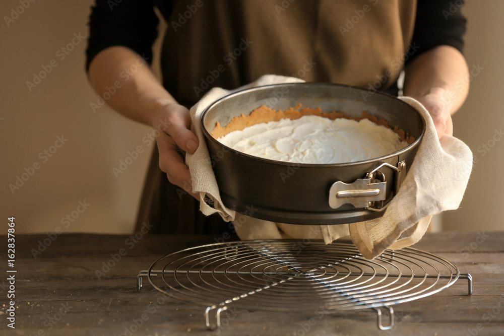 Woman holding baking pan with raw cheese cake in kitchen