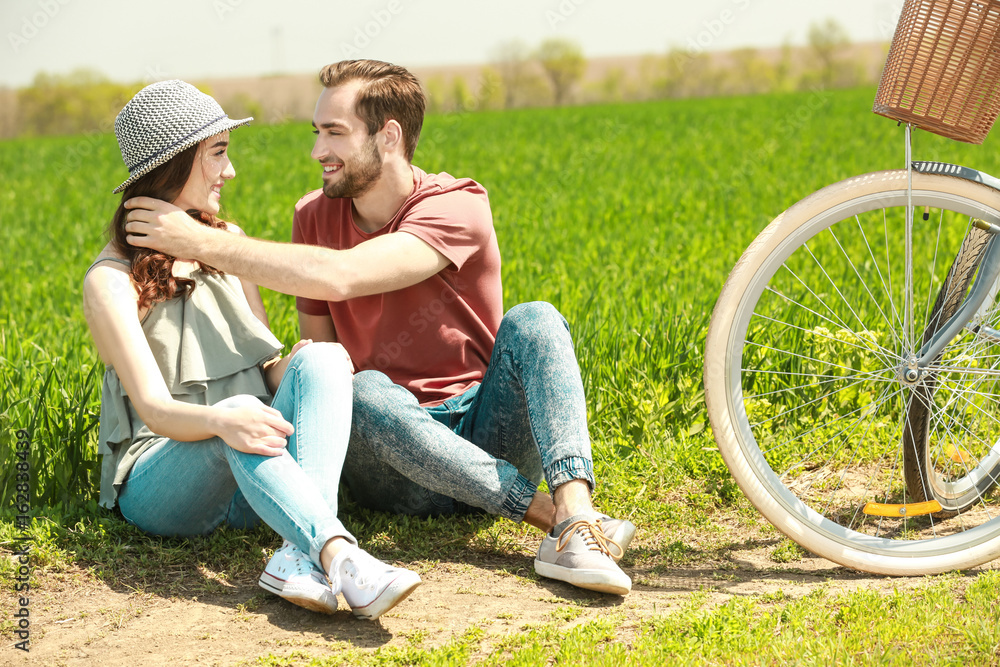 Happy young couple with bicycle sitting on grass in the field