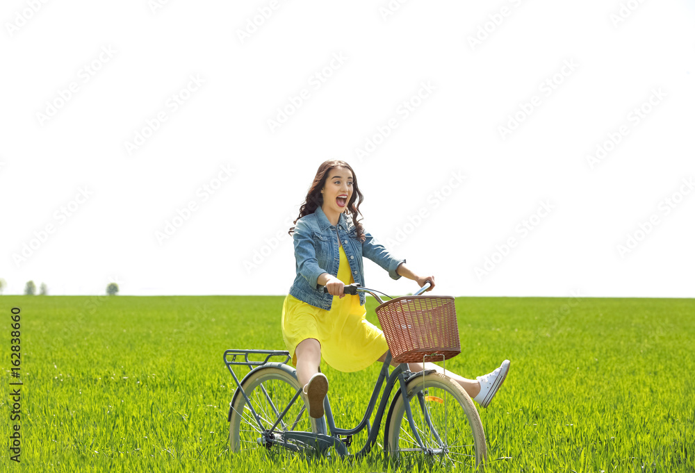 Beautiful young woman with bicycle in green field