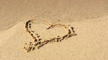 Symbolism For Loosing Or Lost Love.  A Heart Symbol Inscribed In Sand Along Shoreline Washes Away With Incoming Ocean Wave Leaving No Trace