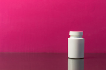 Bottle for pills on a dark glass table. Beautiful pink background.