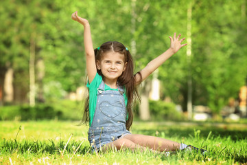 Canvas Print - Cute little girl sitting on green grass in park