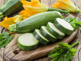 Zucchini with slices and zucchini flowers on a wooden table.