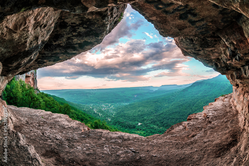 Beautiful scenic summer landscape view of Mezmay village from inside a weird rocky grotto in Caucasus mountains, Lenina Rock shelf, Russia - obrazy, fototapety, plakaty 
