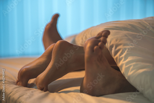 Plakat Nogi pod kołdrą na łóżku