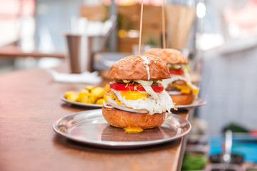 Two Tasty Beef Burgers with tomato, cheese and fried egg on a metal trays on the bar counter waiting to be served. Selective focus, close up. Fast food cafe cuisine. Space for text