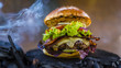 Tasty smoked and grilled beef burger with lettuce, cheese and bacon served with french fries on wooden table with copyspace, smoke mesquite timber wood in background.