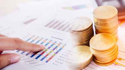 Concept of currency trading. Stack of coins and a hand holding is examining a technical chart of financial instrument. making a decision for an optimal gain. Business and finance concept.