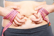 Woman touching stomach holding measuring tape