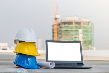 the safety helmet and the blueprint with laptop has white screen isolated at construction site with 