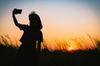 © Korradol - Silhouette of woman taking selfie during sunset with flowering grass