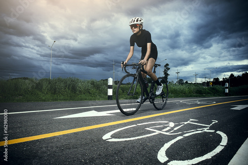 Plakaty Kolarstwo  plakat-na-wymiar-azjatycka-zdrowa-rowerzystka-w-kasku-jazda-na-rowerze-i-cwiczenia-na-rowerze