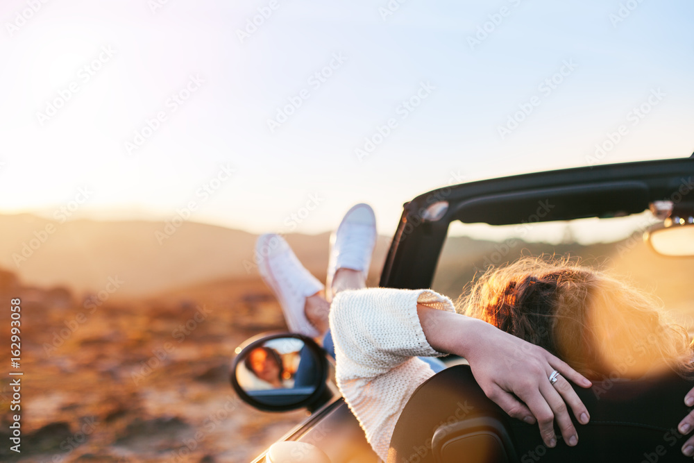 Young woman enjoying the sunset from a convertible - obrazy, fototapety, plakaty 