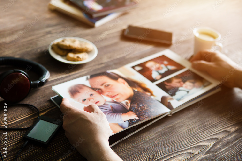 the Hand man holding a family photo album  against the background of the a wooden table
 - obrazy, fototapety, plakaty 