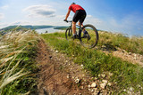 Fototapeta Lawenda - Young cyclist riding mountain bicycle through green meadow against beautiful sky.