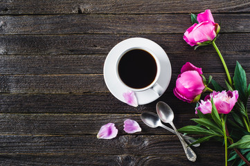 Pink peonies and  white cup of coffee  on a dark wooden background. Breakfast or morning concept