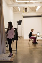 Female Model Standing By Clothes Rack With Photographer Using Laptop