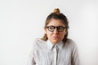 Studioshot of grumpy frowning young female with hair knot and nose-ring wearing glasses making wry face and looking away with unpleasant disgusted expression, showing her negative emotions or disgust