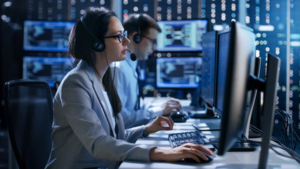 Aufkleber - Female working in a Technical Support Team Gives Instructions with the Help of the Headsets. In the Background People Working and Monitors Show Various Information.
