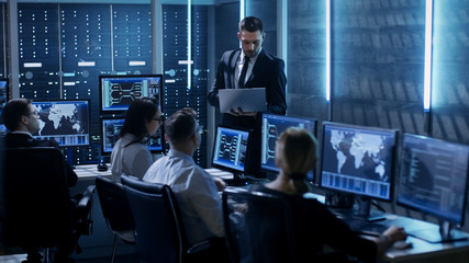 Wall Mural - Professional IT Engineers Working in System Control Center Full of Monitors and Servers. Supervisor Holds Laptop and Holds a Briefing. Possibly Government Agency Conducts Investigation.