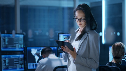 Aufkleber - Young Female Engineer Uses Tablet in System Control Center. In the Background Her Coworkers are at Their Workspaces with many Displays Showing Valuable Data.