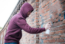 Hooded Tagger Writing Graffiti On Urban Walls