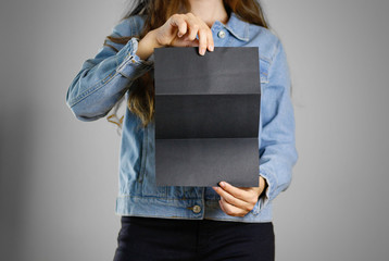 Wall Mural - The girl in the blue denim shirt holds the black empty piece of paper. Ready for your design. Closeup. Isolated