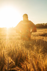 Wall Mural - African woman in traditional clothes walking in a field of crops at sunset or sunrise