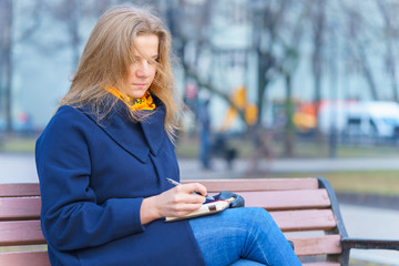 young caucasian woman is writing some idea or letter in her note book, by pen