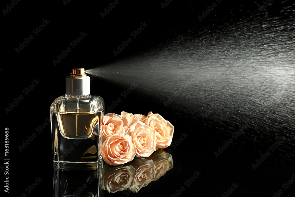 Spraying bottle of perfume and flowers on black background