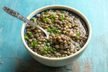 Poster - Bowl with tasty lentil dish and spoon on shabby wooden table, closeup