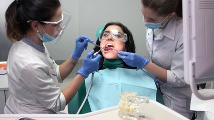 Wall Mural - Two dental doctors at work. Female dentist using water syringe.