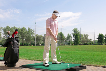 Wall Mural - Young man playing golf on practice range in sunny day