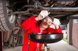 © kolotype - Handsome male car mechanic in uniform working underneath a lifted car and changing motor oil