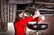 © kolotype - Professional handsome male car mechanic in uniform working underneath a lifted car and changing motor oil