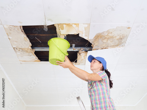 Young Woman Collecting Water In Bucket From Ceiling Ceiling